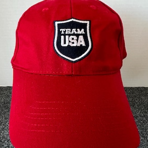 May include: A white ceramic mug with a black handle and the text "But First, Coffee" in a bold, black font. The mug is set against a blurred background, suggesting a cozy setting.