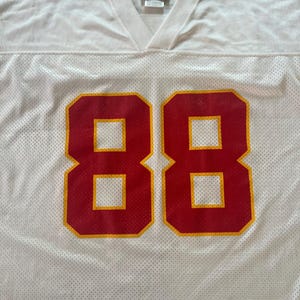 Op de afbeelding: Wit mesh sportshirt met het nummer 88 in rood met gele randen. Het shirt heeft een V-hals en een Puma-logo. De stof heeft een geperforeerde textuur.