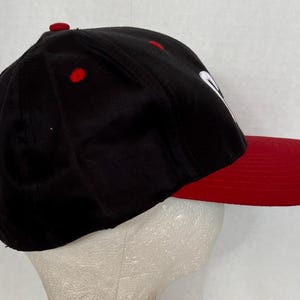 May include: A black and red baseball cap with a white logo. The cap has a curved brim and a mesh back.