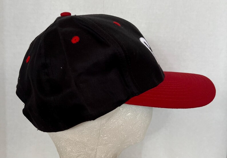 May include: A black and red baseball cap with a white logo. The cap has a curved brim and a mesh back.