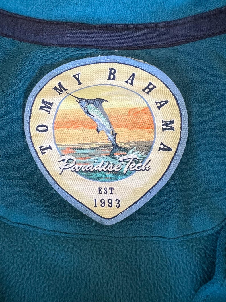 May include: A blue and yellow embroidered patch with the text 'Tommy Bahama Paradise Tech Est. 1993' and a cartoon image of a marlin jumping out of the water.