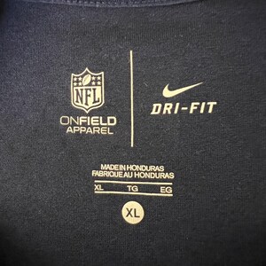 Op de afbeelding: Marineblauw sportshirt met het NFL-logo en het Nike Dri-FIT-logo. Het shirt heeft de tekst "ONFIELD APPAREL" en "MADE IN HONDURAS". De maat is XL.