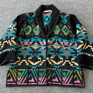 May include: Black jacket with a colorful geometric pattern in teal, pink, yellow, and green. The jacket has a black velvet collar and cuffs, and gold-colored buttons. The design features Aztec-inspired shapes.