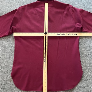 May include: A long-sleeved button-down shirt in a solid deep burgundy color. A wooden T-square measuring tool is placed over the back of the shirt, with the horizontal bar spanning approximately 24 inches and the vertical bar measuring 32 inches.
