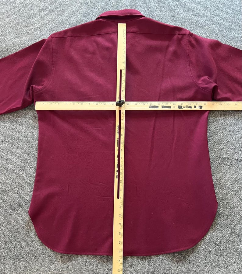 May include: A long-sleeved button-down shirt in a solid deep burgundy color. A wooden T-square measuring tool is placed over the back of the shirt, with the horizontal bar spanning approximately 24 inches and the vertical bar measuring 32 inches.