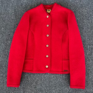 May include: A vibrant red jacket with a round collar and button-down front. The jacket features a tailored fit, decorative stitching, and two front pockets. The sleeves are long, and the jacket is made of a textured fabric.