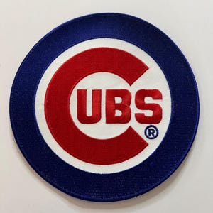 May include: A circular embroidered patch featuring the Chicago Cubs logo. The design consists of a large red letter C with the letters UBS in red inside the curve, set against a white background with a thick blue border and a registered trademark symbol.