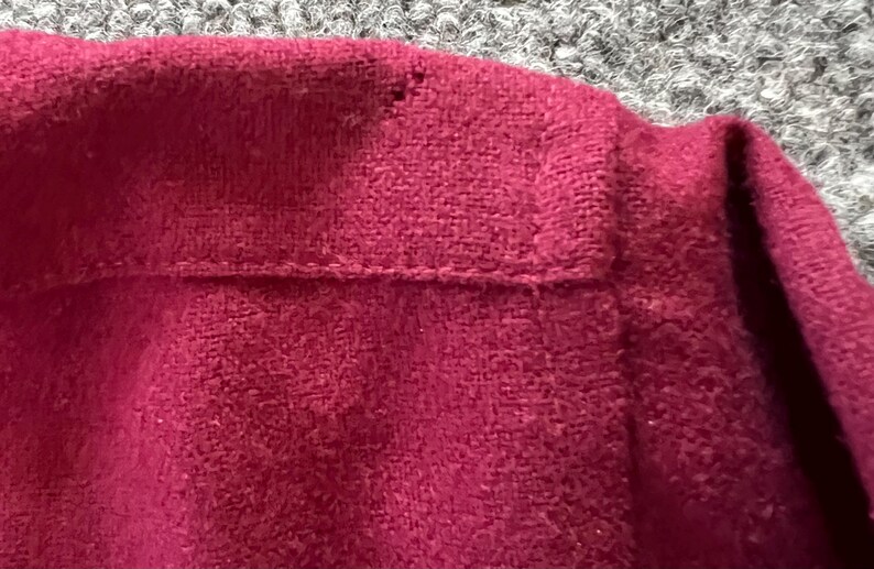 May include: A close-up view of a deep magenta or dark pink garment featuring a textured, soft fabric surface. The item displays a horizontal seam line across the upper section with visible stitching detail and a small, singular snag in the fabric.