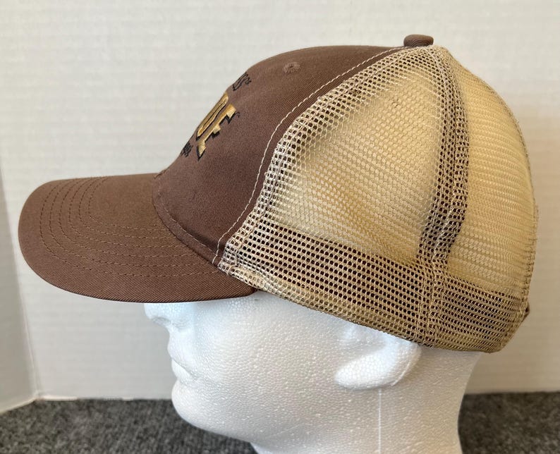 Op de afbeelding: Een bruine baseballcap met een beige mesh achterkant. De cap heeft een gebogen klep en een goudkleurig logo op de voorkant. De cap staat op een witte mannequinhoofd.