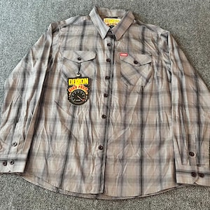May include: A long-sleeved, button-down shirt with a plaid pattern in shades of gray and black. The shirt has two chest pockets and a collar. A tag with the text "DIXON" is attached to the shirt.
