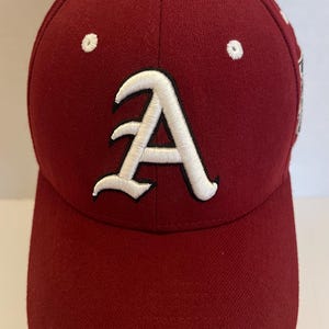 May include: A maroon baseball cap with a white "A" logo embroidered on the front. The cap has a curved brim and a white button on top. The hat is made of a textured fabric.