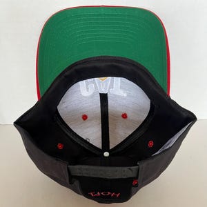 May include: Black and red baseball cap with a white inner lining and the text "JAY" in gold lettering. The cap has a green underside.