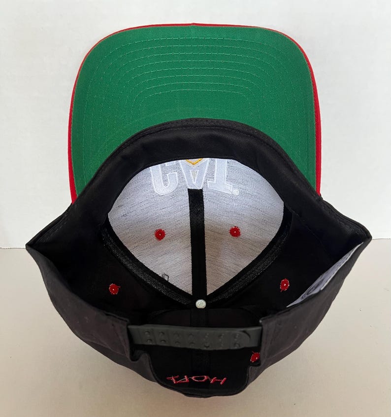 May include: Black and red baseball cap with a white inner lining and the text "JAY" in gold lettering. The cap has a green underside.