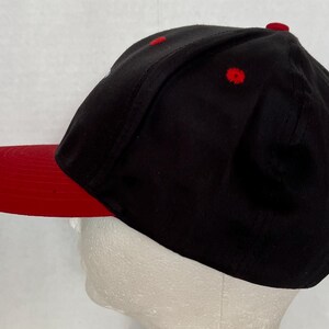 May include: A black and red baseball cap with a red brim. The cap is made of a soft, comfortable fabric.