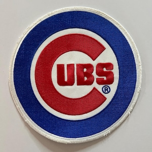 May include: A circular embroidered patch featuring the Chicago Cubs logo. The design consists of a large red letter C enclosing the red text UBS on a white background, surrounded by a thick blue border and a white stitched edge with a registered trademark symbol.