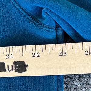 May include: A close-up of a teal blue fabric with a ruler measuring 21 to 24 inches. The ruler is made of wood and has black markings.