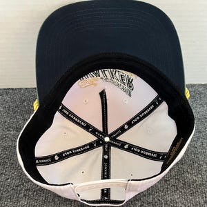 May include: A navy blue and white baseball cap with the text "JOHNNIE WALKER" and "DEVEREUX GOLF" printed on the inside. The cap has a flat brim and a white snapback closure. The cap is a golf accessory.