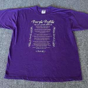May include: A purple t-shirt with the text "Purple Profile" and a list of characteristics in white. The shirt is made of a soft material and has short sleeves. The text is centered on the front of the shirt.