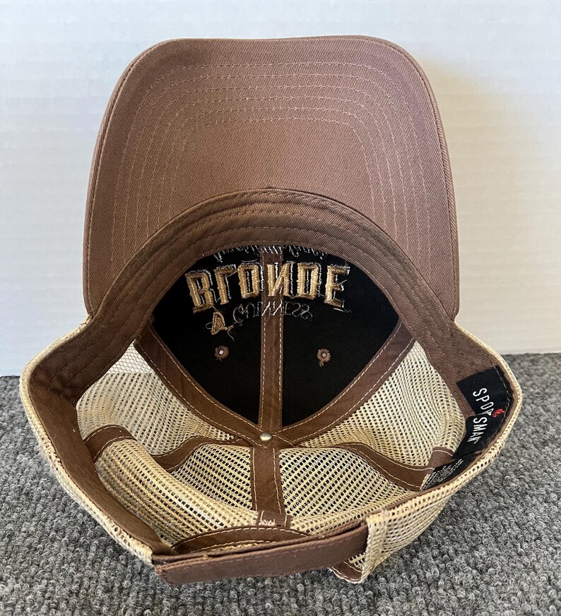 Op de afbeelding: Bruine baseballcap met een mesh achterkant en een gebogen klep. De binnenkant heeft het woord "BLONDE" geborduurd in gouddraad op een zwarte achtergrond. De cap heeft een druksluiting.