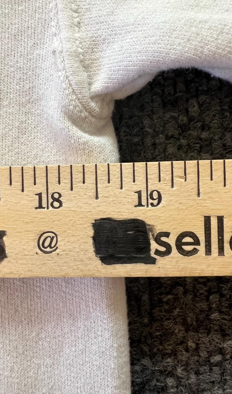 Peut inclure: Un v&ecirc;tement en tissu blanc plac&eacute; derri&egrave;re une r&egrave;gle en bois. La r&egrave;gle affiche les chiffres 18 et 19, avec le texte @ et sell visible sous les chiffres. La r&egrave;gle indique une mesure allant de 45,7 cm &agrave; plus de 48,3 cm.