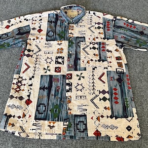 May include: Short-sleeved button-down shirt with a cream-colored background and a colorful geometric pattern. The pattern includes blue, red, yellow, and green shapes. The shirt has a collared neckline and a button-up front.