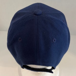Pu&ograve; includere: Un berretto da baseball blu navy con una cinghia regolabile nera sul retro.