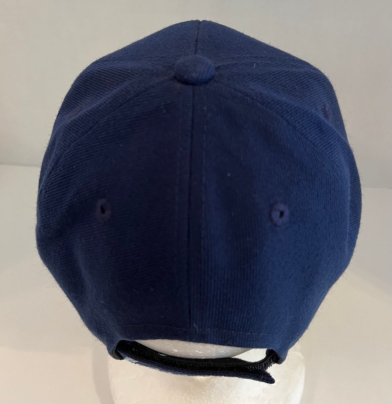 Pu&ograve; includere: Un berretto da baseball blu navy con una cinghia regolabile nera sul retro.