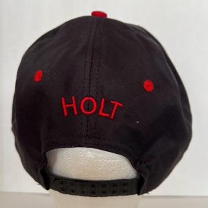 May include: Black and red baseball cap with the word "HOLT" embroidered in red on the front.