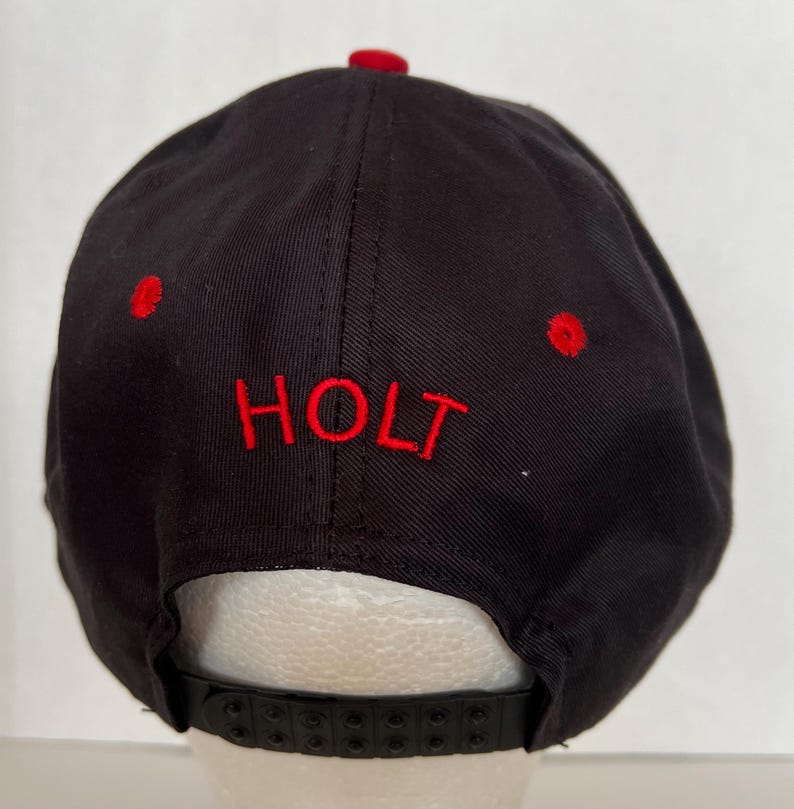 May include: Black and red baseball cap with the word "HOLT" embroidered in red on the front.