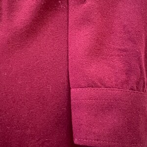 May include: A solid deep magenta long-sleeve shirt featuring a structured cuff with visible stitching. The fabric has a soft, matte texture and a consistent, uniform color throughout the sleeve and the cuff area, showcasing a clean design.