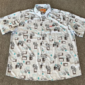 May include: A white short-sleeved button-down shirt with a blue and gray bicycle print. The shirt has a pocket on the left side with the word "Dixon" printed in orange.