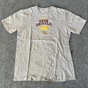 Pu&ograve; includere: T-shirt grigio melange con la scritta "SUN DEVILS 1995" in bordeaux e oro. Il logo Nike &egrave; sopra il testo. La maglietta &egrave; a maniche corte e ha un girocollo.