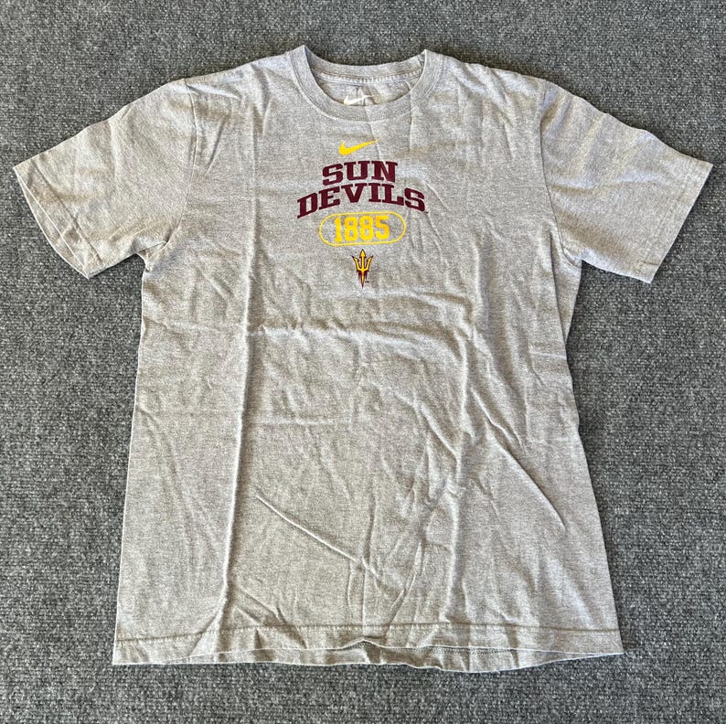 Pu&ograve; includere: T-shirt grigio melange con la scritta "SUN DEVILS 1995" in bordeaux e oro. Il logo Nike &egrave; sopra il testo. La maglietta &egrave; a maniche corte e ha un girocollo.