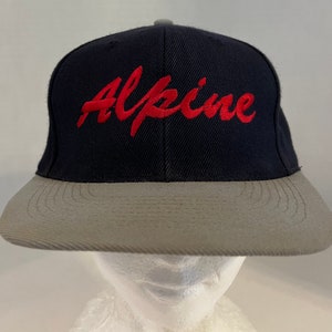 May include: A navy blue and gray baseball cap with the word "Alpine" embroidered in red on the front.