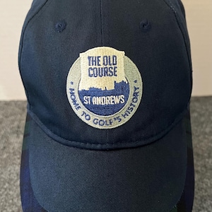 May include: Navy blue baseball cap with a curved brim featuring a green and blue plaid pattern. The cap has an embroidered patch with the text "THE OLD COURSE ST ANDREWS HOME TO GOLF'S HISTORY".
