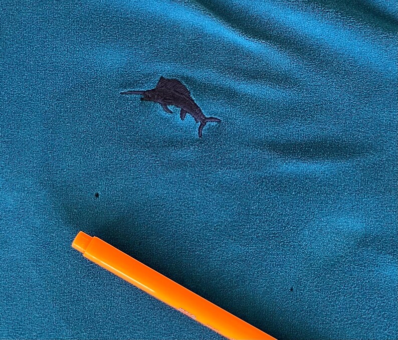 May include: A teal blue fabric with a black embroidered marlin fish design.