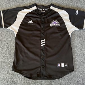 May include: Black and white baseball jersey with the Adidas logo, Colorado Rockies logo, and the words "Colorado Rockies" on the front. The jersey has a white stripe down the front and white sleeves.
