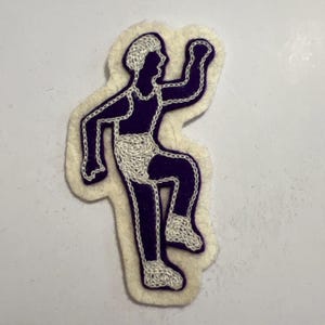 May include: A purple felt patch featuring a white embroidered outline of a person running. The figure is depicted in a dynamic pose with one leg raised and arms bent. The white embroidery highlights the hair, shorts, and shoes against the purple.