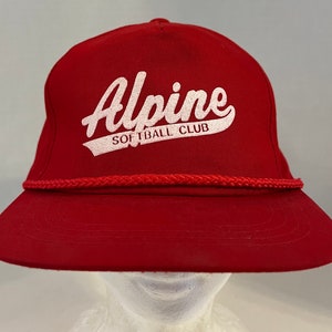 May include: Red baseball cap with a white rope trim and the text "Alpine Softball Club" in white.