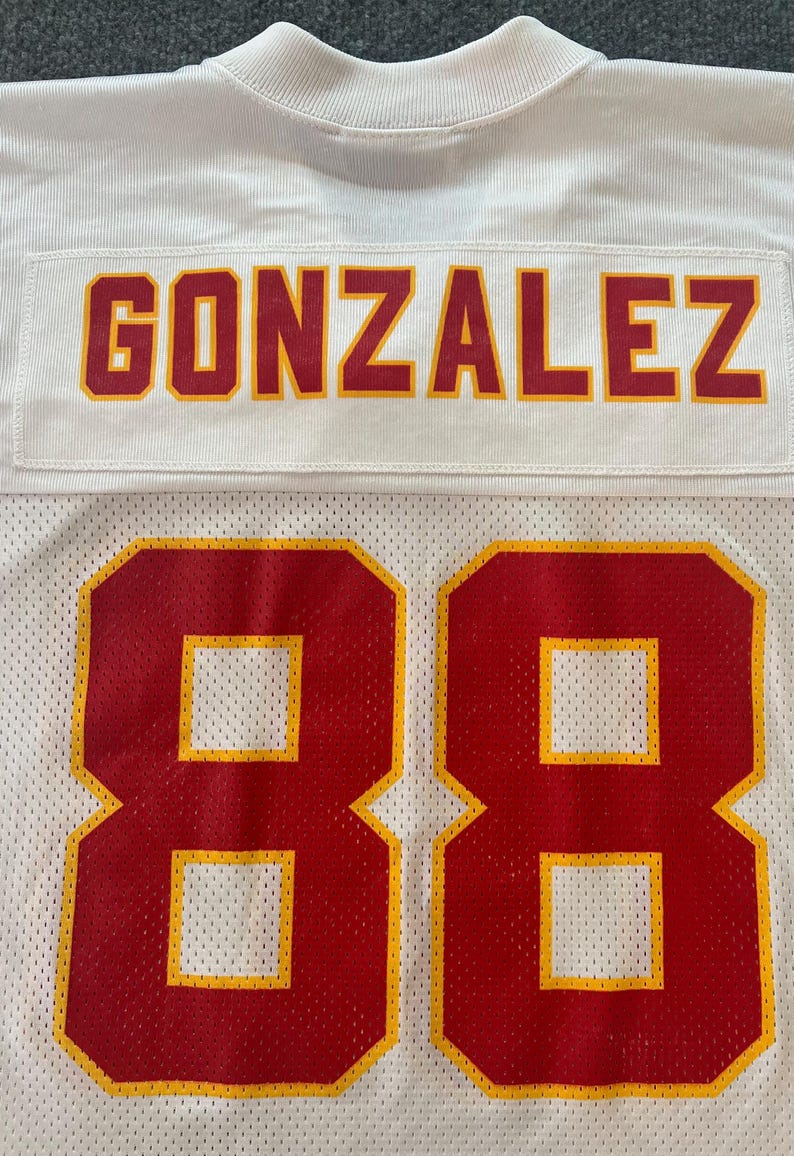 Op de afbeelding: Wit mesh sportshirt met de naam "GONZALEZ" in rode en gouden letters. Het nummer "88" staat in grote rode en gouden cijfers op het onderste deel van het shirt.
