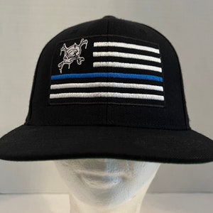 May include: Black baseball cap with a thin blue line American flag and a skull graphic on the front.