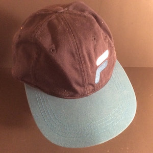 May include: A black and teal baseball cap with a white and blue logo on the front. The logo is a stylized letter "F".