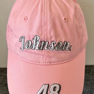 May include: A pink baseball cap with the name "Johnson" embroidered in white script across the front. The number "48" is embroidered in white with a black outline on the brim. The cap is made of a soft fabric.