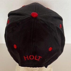 May include: Black baseball cap with red stitching and the word "HOLT" embroidered in red on the back.