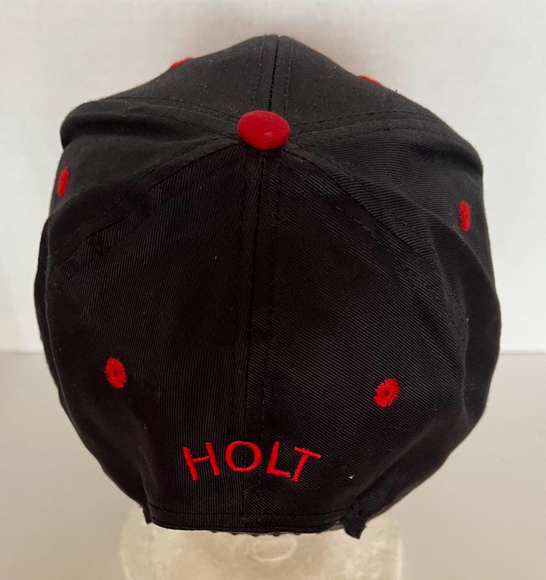 May include: Black baseball cap with red stitching and the word "HOLT" embroidered in red on the back.