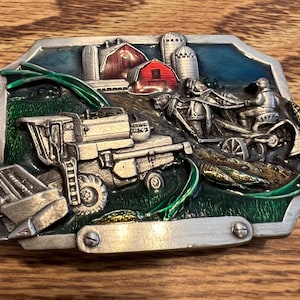 May include: A silver belt buckle with a green, blue, and red enamel design. The buckle depicts a farm scene with a combine harvester, a horse-drawn plow, and a red barn.