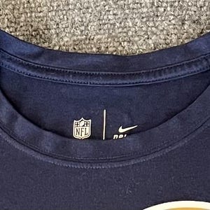 Op de afbeelding: Marineblauw T-shirt met ronde hals, NFL-logo en Nike swoosh. Het shirt heeft een klassiek design en is gemaakt van een zacht, comfortabel materiaal. Geschikt voor casual wear.