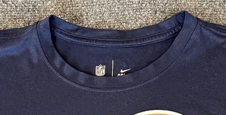 Op de afbeelding: Marineblauw T-shirt met ronde hals, NFL-logo en Nike swoosh. Het shirt heeft een klassiek design en is gemaakt van een zacht, comfortabel materiaal. Geschikt voor casual wear.