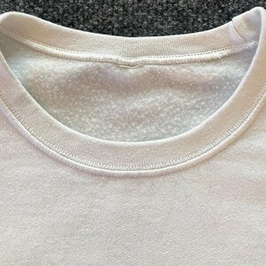 Peut inclure: Un sweat-shirt blanc &agrave; col rond dot&eacute; d'un col c&ocirc;tel&eacute; et d'un int&eacute;rieur en polaire douce. Le v&ecirc;tement est fabriqu&eacute; dans un tissu blanc uni avec une texture uniforme, pr&eacute;sentant une coupe classique &agrave; enfiler par-dessus la t&ecirc;te.