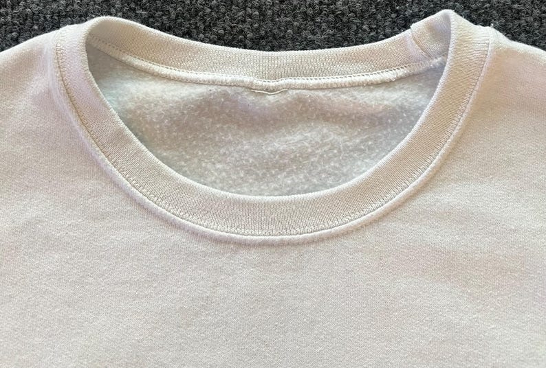 Peut inclure: Un sweat-shirt blanc &agrave; col rond dot&eacute; d'un col c&ocirc;tel&eacute; et d'un int&eacute;rieur en polaire douce. Le v&ecirc;tement est fabriqu&eacute; dans un tissu blanc uni avec une texture uniforme, pr&eacute;sentant une coupe classique &agrave; enfiler par-dessus la t&ecirc;te.